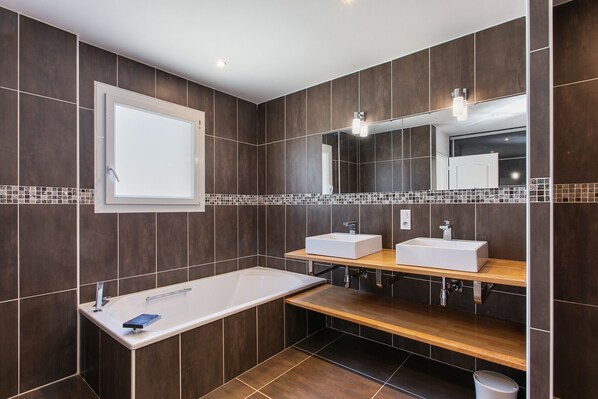 A modern bathroom with a large bathtub, two sinks, a mirror, and a wooden vanity.