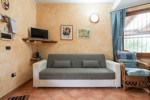A living room with a sofa, a television, a wicker chair, and two framed pictures on the wall. - Holiday Home 'Brezza Di Mare' with Sea View, Private Terrace and Air Conditioning (Calasetta)