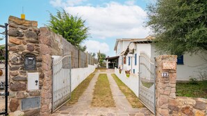 Un chemin de pierre mène à une entrée fermée par un portail, avec un bâtiment blanc et un portail en métal.