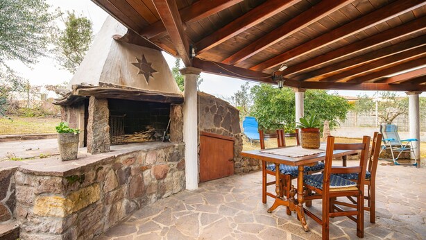 Une terrasse extérieure avec une cheminée en pierre, une table en bois et des chaises.