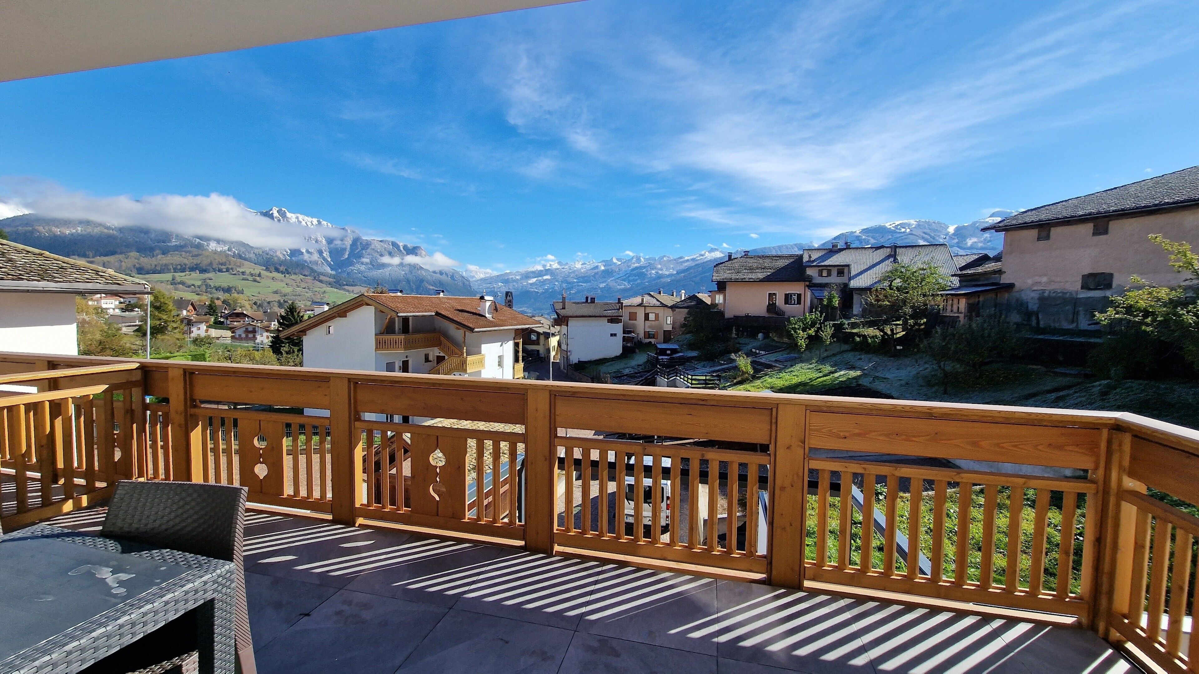 Un balcon en bois offrant une vue sur une chaîne de montagnes et des immeubles d’habitation.