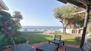 A patio with wooden tables and chairs, a view of the sea, and a garden with plants and a tree. - Villa 'Costa Dei Monaci Villas - Tropea' with Sea View, Wi-Fi and Air Conditioning (Costa dei Monaci)