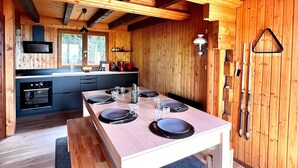 Un intérieur en bois avec une table à manger pour quatre personnes, une cuisine équipée d’appareils électroménagers modernes et une grande fenêtre.