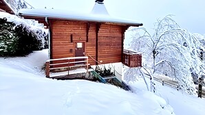 Une cabane en bois avec un toit enneigé, une porte en bois et un petit porche.