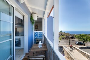 A balcony with a wooden table, a white lantern, and a view of the ocean.