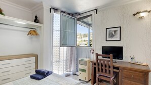 Een slaapkamer met een bed, een bureau, een stoel, een televisie en een raam met gordijnen.