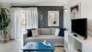 Een woonkamer met een bank, een salontafel, een televisie en een groot raam met gordijnen.