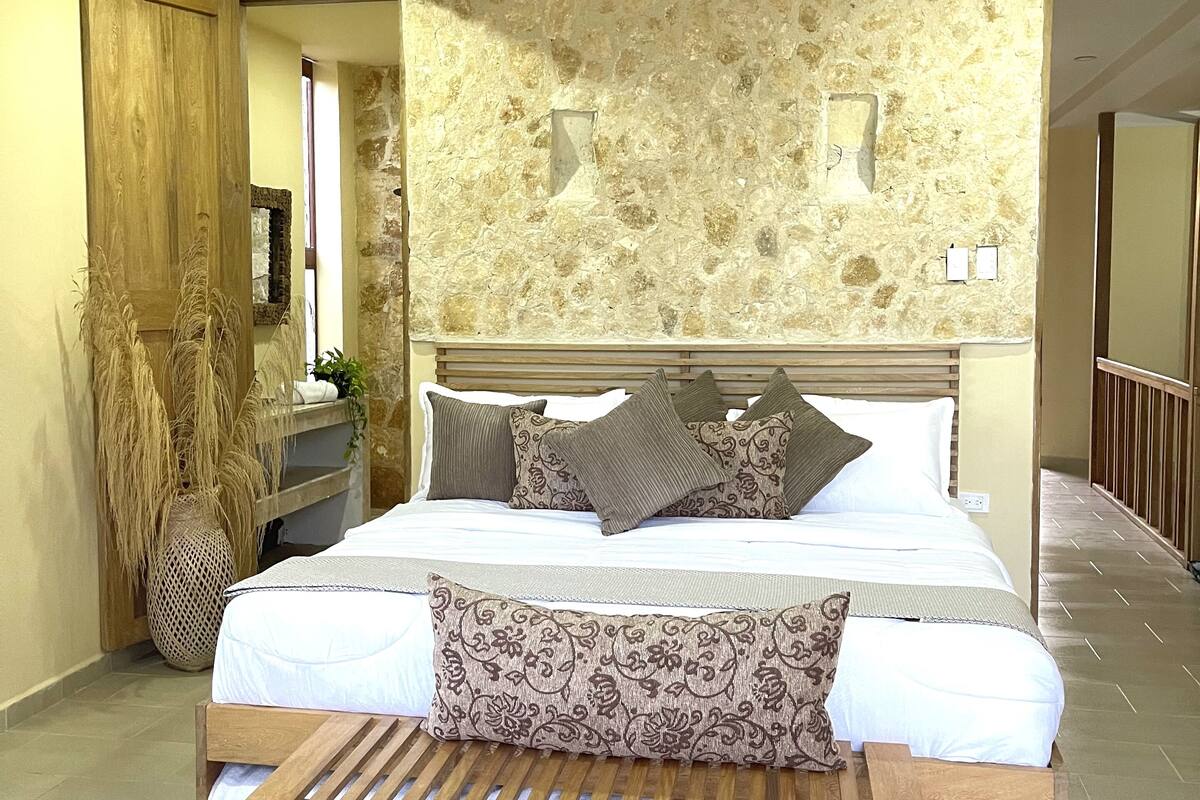 A bedroom with a bed, a wooden bench, a ceiling fan, and a stone wall.