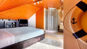 Ein Schlafzimmer mit Holzbalkendecke, einem Bett, einem Fernseher, einem Schreibtisch und einer begehbaren Dusche.