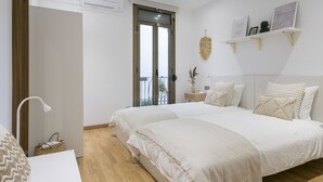 Un dormitorio con dos camas, una mesita de noche, una planta colgante y una ventana con vistas.