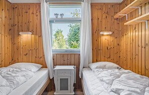 Two single beds with white bedding, a radiator, and a window with a view of greenery.