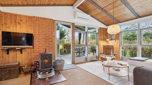 A cozy living room with a fireplace, a TV, and a large window overlooking a garden.