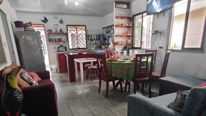 A living room with a sofa, a dining table with chairs, a kitchen area with a refrigerator, and a TV mounted on the wall. - Green House Casa de Playa Tortuguero (Colorado)