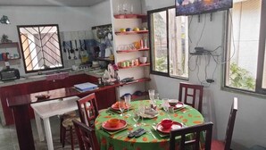 A dining area with a round table set for four, surrounded by wooden chairs. A television is mounted on the wall above the table. - Green House Casa de Playa Tortuguero (Colorado)