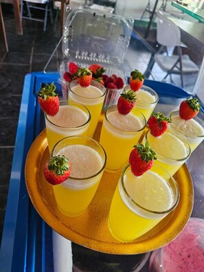 A tray with several glasses of a yellow beverage, each garnished with a strawberry, on a blue table. - Green House Casa de Playa Tortuguero (Colorado)