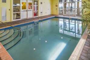 Ein Hallenbad mit klar blauem Wasser, einer gefliesten Poolumrandung und Blick auf den Ozean durch Glastüren.