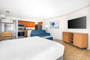 A hotel room with a bed, kitchenette, blue sofa, TV, and a painting.