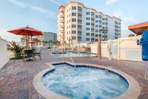 A hot tub area with a pool, outdoor seating, and a building in the background.