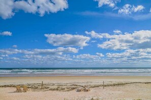A beach with a clear sky, waves, and two empty beach chairs.