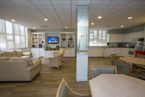 Ein geräumiger Wohnbereich mit einer Couch, Sesseln, einem Fernseher und einer Küchenzeile mit Schränken und einem Esstisch.