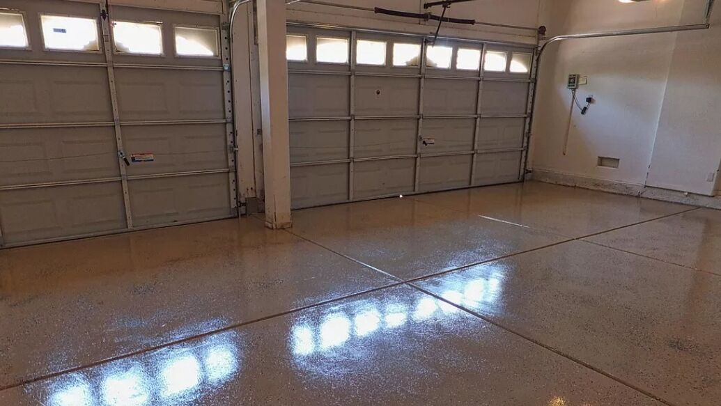 A garage with two large metal garage doors, a concrete floor, and a wall-mounted electrical box.