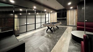 Un espacio moderno con mesa de billar, asientos acolchados y un amplio ventanal con persianas.