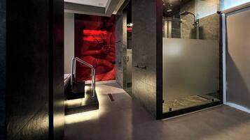 Une salle de bain moderne avec une douche à parois de verre, un porte-serviettes apparent et un mur d’accent rouge.