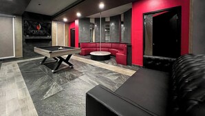 Un espacio lounge moderno con mesa de billar, asientos rojos y una mesa de carambola.