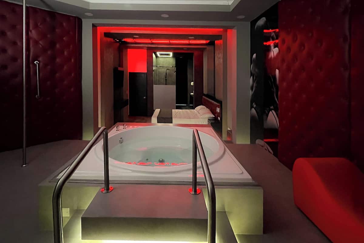 A modern spa room with a large bathtub, a seating area, and a red-lit wall.