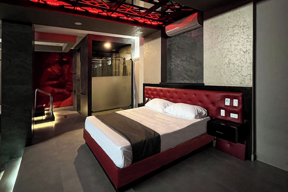 A modern hotel room with a red upholstered headboard, a large bed, a walk-in closet, and a red-lit ceiling.