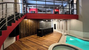 Un interior moderno con suelo de madera, una zona de bar, una piscina y una escalera.