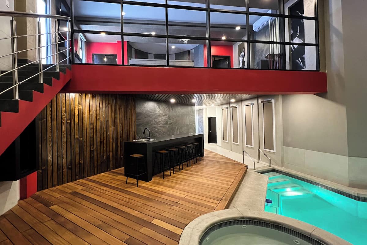 A modern interior with a wooden floor, a bar area, a pool, and a staircase.