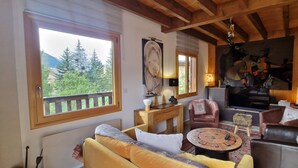 A cozy living room with a sofa, armchairs, a coffee table, and a fireplace. There is a large window with a view of trees and mountains. - Warm chalet for 6 people, Saint-Chaffrey (Saint-Chaffrey)