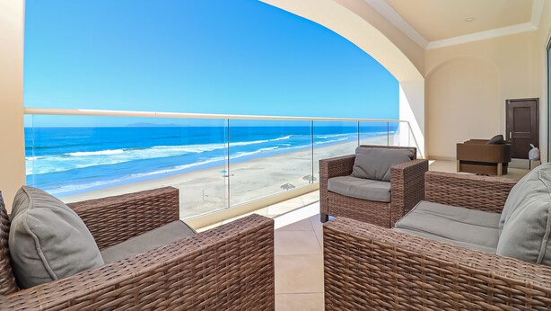 Un balcón con mobiliario de mimbre, vista a la playa y una puerta a la derecha.