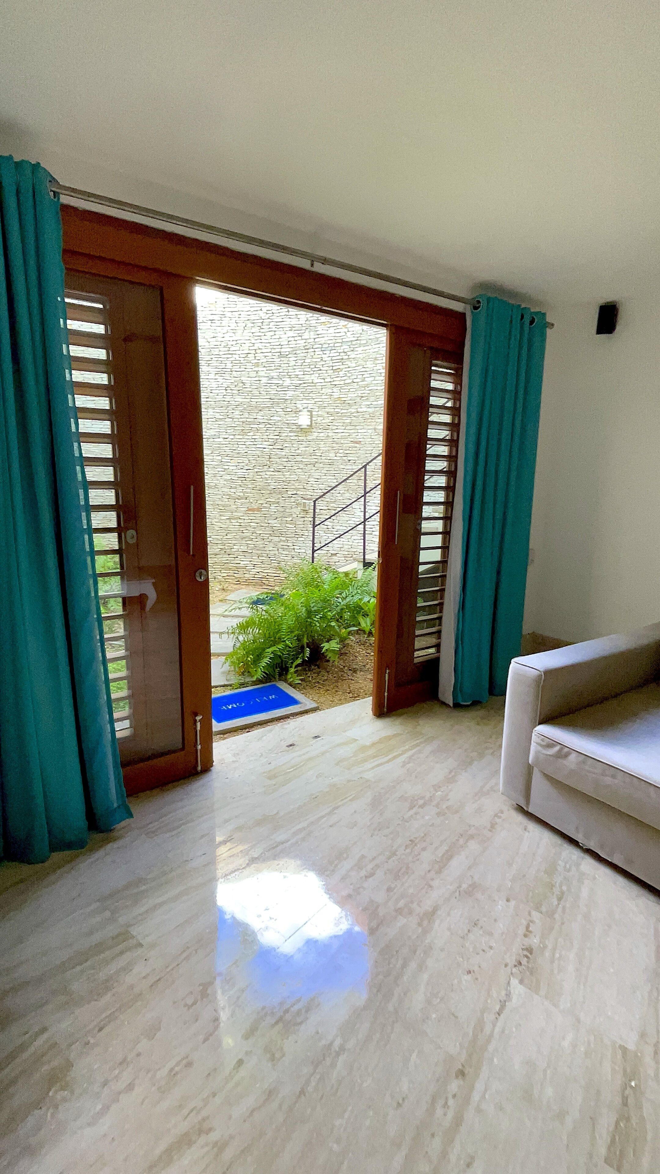 Quarto com sofá branco, porta de madeira que dá para uma parede de pedra, e área externa azul.