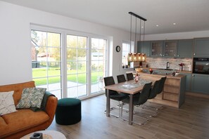 Una cocina moderna con ventanas amplias, un comedor con mesa y sillas, y una sala de estar acogedora con un sofá y un reposapiés.