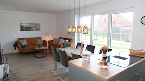 A modern kitchen with a dining area, featuring a wooden table, chairs, and a built-in island with a fruit bowl.