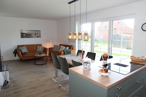 A modern kitchen with a dining area, featuring a wooden table, chairs, and a built-in island with a fruit bowl.
