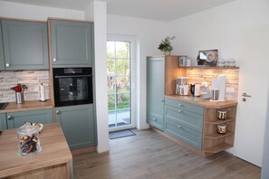 A modern kitchen with light blue cabinets, a wooden countertop, and a built-in oven. There is a window providing a view of the outdoors.