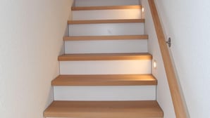 A staircase with wooden steps and a handrail, leading to a room with a window.