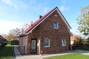 A brick house with a red roof, a green door, and a small front yard.
