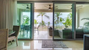 Una habitación moderna con una puerta de vidrio que da a un balcón con vistas a palmeras y al océano.