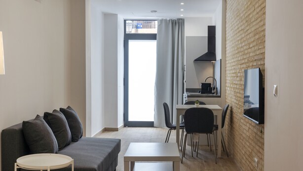 Un salon moderne avec un canapé gris, une petite table ronde et un coin cuisine comprenant une table à manger et des chaises.