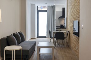 Un saló modern amb un sofà gris, una taula rodona petita i una zona de cuina amb una taula de dinar i cadires.