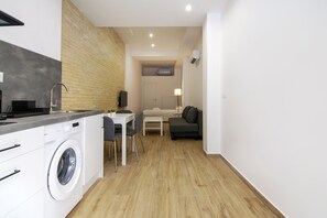 A compact living space with a washing machine, a small dining table, a sofa, and a TV. - VLC HOST - Fray Pedro E (Valencia)