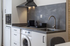 A compact kitchen with a washing machine, a microwave, a coffee maker, and a modern faucet. - VLC HOST - Fray Pedro E (Valencia)