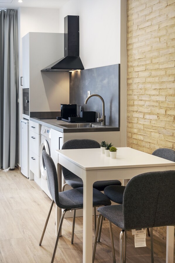 A modern kitchen with a built-in oven, a black range hood, and a stainless steel sink. There is a dining table with four chairs and a small potted plant on it. - VLC HOST - Fray Pedro E (Valencia)