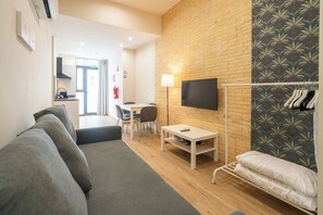 A modern living room with a sofa, a small table, a TV mounted on a brick wall, and a clothing rack. - VLC HOST - Fray Pedro E (Valencia)
