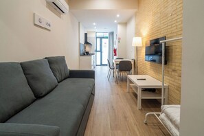 A modern hotel room with a grey sofa, a TV mounted on the wall, a bedside table, and a wooden floor. - VLC HOST - Fray Pedro E (Valencia)