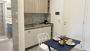 Una kitchenette compacta con un lavamanos, una cafetera y un pequeño comedor con mesa y sillas.